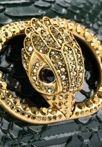 Złota i czarna zapięcie ozdobione klejnotami, z wyróżniającym się szczegółowym teksturowanym wzorem, na błyszczącym zielonym tle w motyw reptilian.