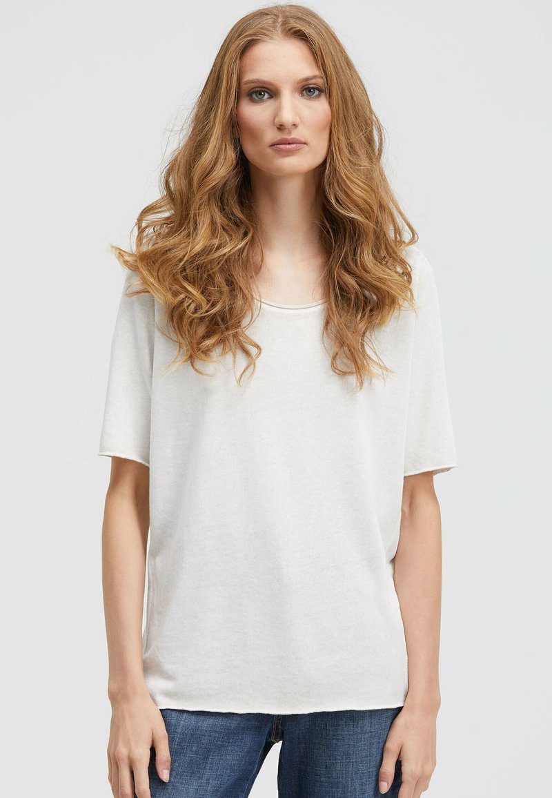 Helles beige T-Shirt mit kurzen Ärmeln und rundem Ausschnitt, aus weichem Stoff. Kombiniert mit blauen Jeans. Lässiger, lockerer Schnitt.