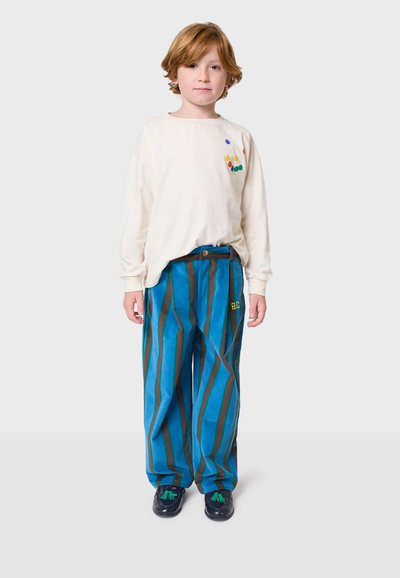 Kremasta košulja dugih rukava s šarenim točkicama, uparena s plavim hlačama s vertikalnim prugama i crnim cipelama s zelenim akcentima.