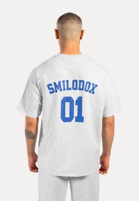 Szara, oversize koszulka z krótkim rękawem z niebieskim nadrukiem "SMILODOX" i numerem "01" na plecach. Wykonana z bawełny.
