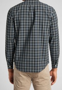 Camicia a maniche lunghe a quadri in blu scuro, grigio e nero; presenta un colletto a bottone, una piega singola sul retro e polsini con bottone.