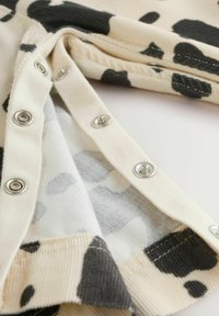 Bawełniana tkanina o kremowym tle z czarnym i szarym wzorem w krowi cętki. Funkcjonalne zatrzaski zdobią dół, którym charakteryzuje się delikatna prążkowana tekstura.