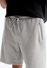 Shorts gris en tissu texturé, dotés d'une taille élastique avec cordon de serrage et d'une poche zippée sur le côté pour un rangement sécurisé.