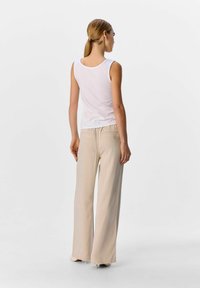 Hvid ribbet tanktop kombineret med lyse beige vidde bukser. Glat stofstruktur, afslappet pasform og diskret baglomme detalje.