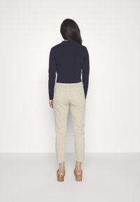 Top de manga larga de color marino combinado con pantalones ajustados color crema, que muestran un diseño pulido y zapatos de tacón de bloque de madera.