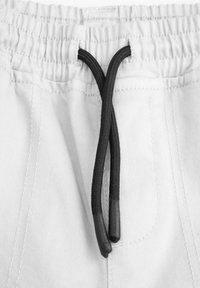 Białe szorty z elastycznym pasem i czarnym sznurkiem. Cechy to widoczne szwy oraz teksturowana powierzchnia materiału.