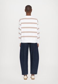 Hvit skjorte med lange ermer og beige horisontale striper, kombinert med løse mørke denimbukser og lyse sko.