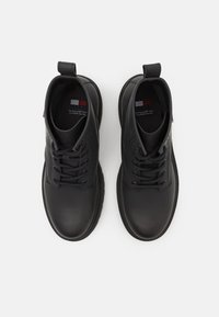 Svarta läderskor med rund tå, snördesign och dragflik vid hälen; texturerad yta och platt gummisula.