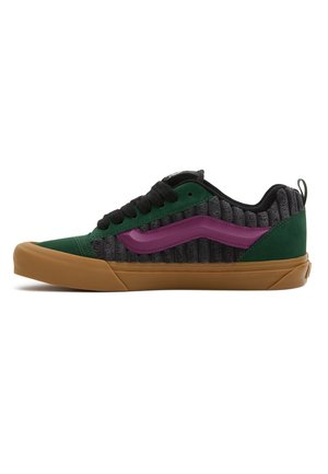 Low-top sneaker with green suede, grey corduroy sides, purple side stripe, black laces, and gum rubber sole.