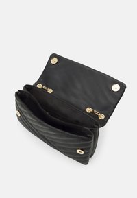 Svart quiltad läderhandväska med guldfärgad metalldetaljer, utrustad med magnetlås och två innerfack separerade av ett tygskiljevägg.