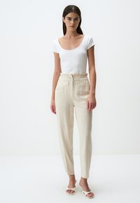 Top blanc à rayures et à manches courtes associé à un pantalon beige à taille haute avec une ceinture froncée et des poches latérales. Sandales à talons ouvertes.