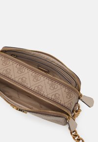 Lille beige crossover-taske med guld lynlåse, kædestrop og flere rum, inklusive en lynlåsindvendig lomme.