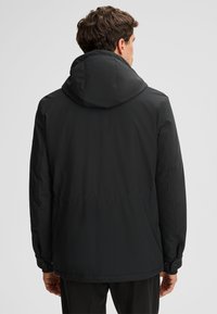Czarna kurtka wierzchnia z kapturem, wykonana z gładkiej tkaniny o matowym wykończeniu, z regulowanymi mankietami zapinanymi na guziki. Prosty, elegancki fason bez zdobień.