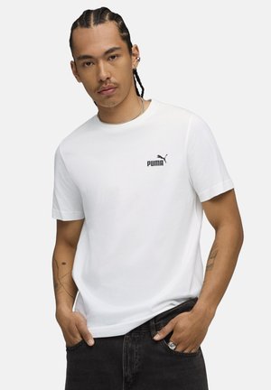 Hvid bomulds T-shirt med korte ærmer, prydet med et sort Puma-logo på venstre bryst, kombineret med mørk denimjeans.