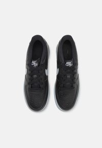 Juoda Nike Air Force 1 avalynė su lygaus odos paviršiumi, perforuotu pirštu ir kontrastingu balto logotipo akcentu. Apsirūpinusi juodomis šniūromis ir pilkos gumos padu.