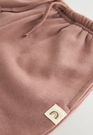 Rosa Fleece-Shorts mit elastischem Bund und Kordelzug sowie einem gestickten Etikett, das ein Regenbogen-Icon zeigt. Weiche Textur überall.
