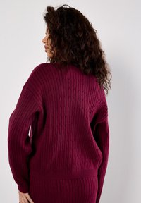 Burgundské pletené svetr s vertikálním žebrováním, oversized rukávy a uvolněný střih. Bez zapínání nebo viditelných vzorů.