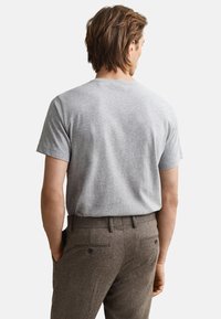 Siva bombažna majica s kratkimi rokavi in okroglim vratom, kombinirana s rjavimi hlačami v ribji kosti z zadnjimi žepi in detajli z gumbi.