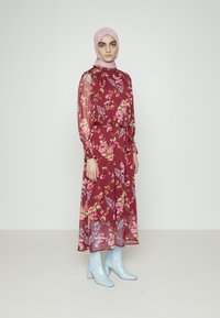 Vestido floral em burgundy com mangas longas transparentes, uma cintura franzida e uma saia esvoaçante. Combinado com botas de salto azul claro e um hijab correspondente.