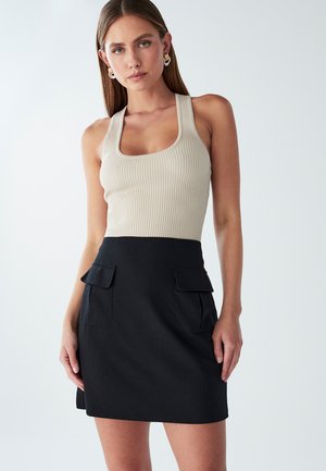 Beige ribbed tank top with a square neckline paired with a black skirt featuring two front patch pockets and a straight silhouette.