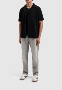 Zwarte korte mouwen overhemd met een gestructureerde stof, gecombineerd met een aansluitend zwart t-shirt, lichtgrijze jeans en witte sneakers met zwarte accenten.