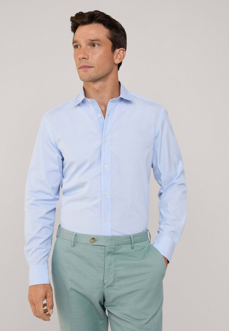 Lichtblauwe blouse met lange mouwen en een button-down kraag, gemaakt van een gladde stof. Gecombineerd met lichtgroene broek, met een knoopdetail.