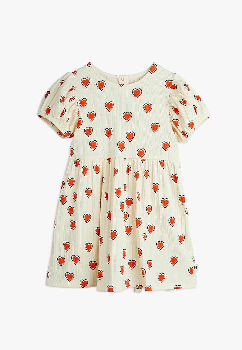 Trumpas rankovės suknelė, pagaminta iš smulkios grietinėlės medžiagos, su raštu, kuriame pavaizduoti raudoni ir juodi širdelės kontūrai. Plataus silueto sijonas su uždarymu nugaros mygtuku.