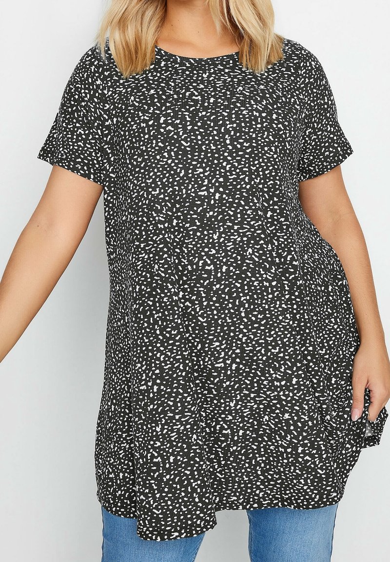 Svart tunika med vitt prickigt mönster, korta ärmar och avslappnad passform; mjukt tyg med subtil textur, kombinerad med blåjeans.