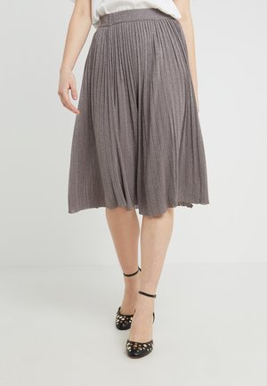 Jupe midi plissée grise en tissu scintillant ; taille élastique ; portée avec des chaussures à bride de cheville noires ornées de clous dorés.