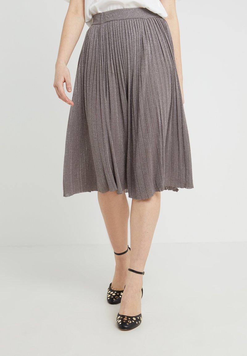 Gonna midi plissettata grigia realizzata in tessuto luccicante; vita elastica; indossata con scarpe nere con cinturino alla caviglia dotate di borchie dorate.