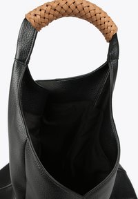 Sac fourre-tout en cuir noir avec une anse tressée beige. Design à ouverture supérieure, extérieur texturé et doublure intérieure spacieuse en noir.