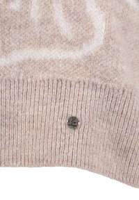 Lichtbeige gebreide trui met een geribbelde zoom. Bevat een ronde metalen tag met een hartontwerp en tekst. Zachte textuur met een subtiel patroon.