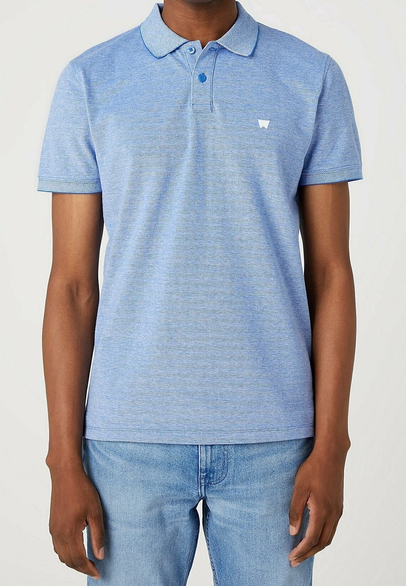 Polo bleu clair en tissu texturé, avec une patte de boutonnage, des manches courtes et un petit logo blanc sur la poitrine.