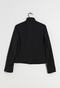 Schwarze Jacke mit hohem Kragen, langen Ärmeln und strukturierter Passform. Mit Reißverschluss an den Ärmeln und einer glatten, matten Stoffoberfläche.