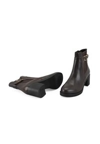 Bottines en cuir marron avec une boucle sur le côté, bout carré et talon bloc, dotées d'une texture lisse et de panneaux élastiques sur les côtés pour un enfilage facile.