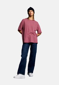Striped red and white oversized t-shirt paired with dark blue jeans and white sneakers, worn with a black beanie. Casual, relaxed fit.