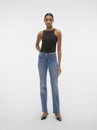 Body preto sem mangas, com decote alto, emparelhado com jeans retos de tom azul claro com desbotamento sutil, e sapatos de salto alto pretos de bico fino.