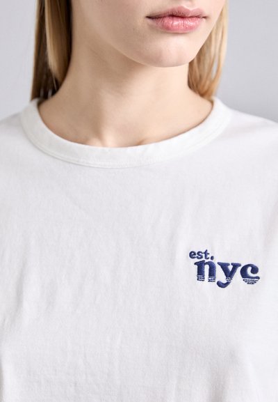 White cotton t-shirt featuring a navy blue embroidered graphic that reads "est, NYC." Classic crew neck design with a soft texture.