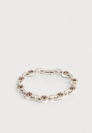 Stříbrný náramek s kulatými hnědými drahokamy obklopenými malými průhlednými krystaly, zasazený do propojených kruhových a vlnitých vzorů.