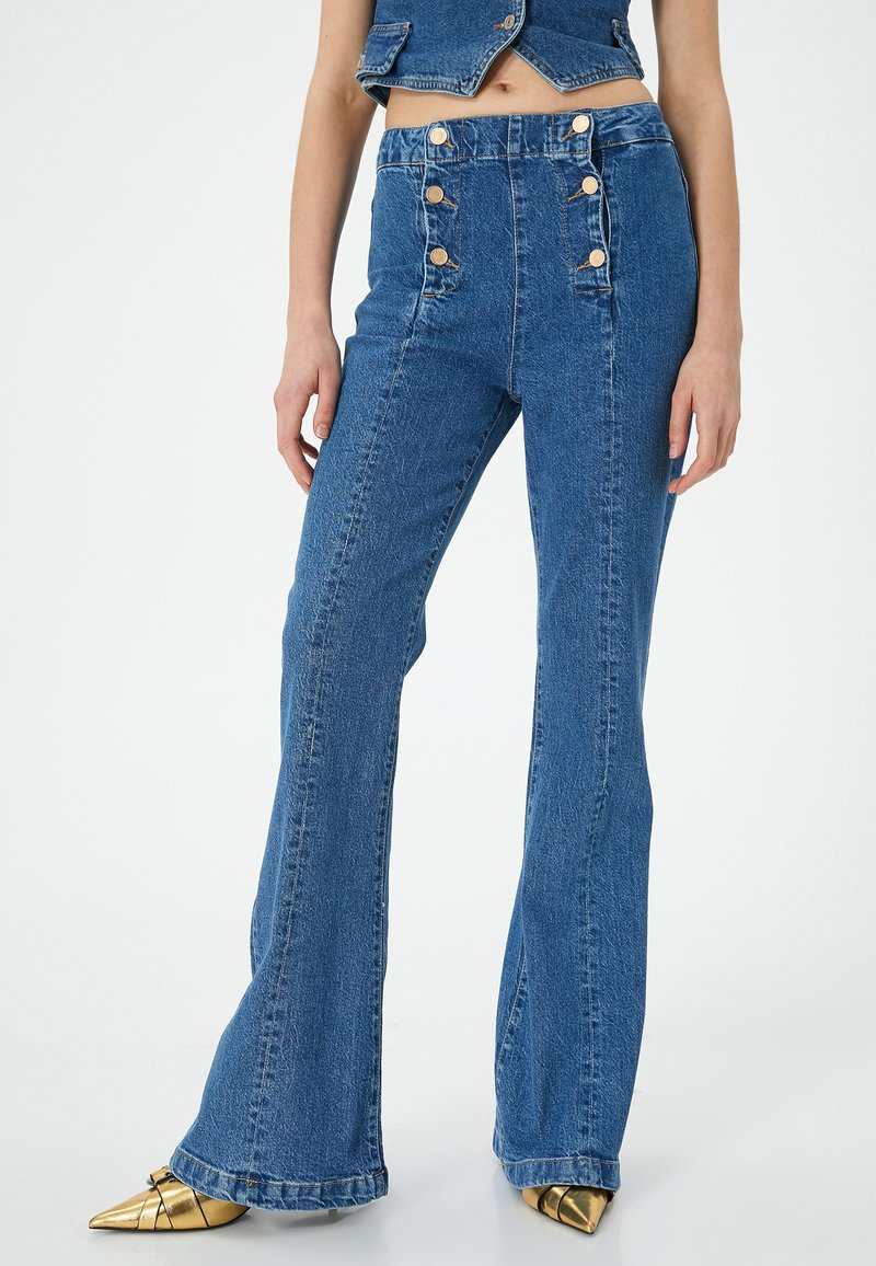 Högmidjade utsvängda jeans i medelblå denim med detaljer i guld, sydda accenter och en lätt blekt yta.