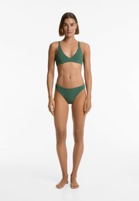 Grön bikini-set med texturerad yta, triangulärt topp med breda remmar och lågt skurna bottoms. Slätt material med minimal design.