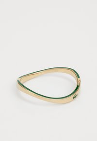Kuldtono bangles käevõru, millel on roheline emailiga vooder ja Lacoste logo aksent. Sile tekstuur ja kitsenev, nurga kujuline disain.