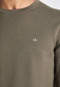 Camicia a maniche lunghe in verde oliva con texture, colletto tondo e piccolo logo "ck" bianco sul petto sinistro.