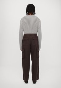 Harmaa ribbineuloksinen neule pitkähihaisilla hihoilla, yhdistetty tummanruskeisiin cargo-housuihin, joissa on isot sivutaskut ja rento istuvuus.