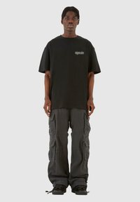 Sort oversized t-shirt med logo på brystet, parret med grå cargo bukser med flere lommer og en afslappet pasform. Sorte sneakers.
