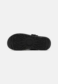 Black shoe sole featuring a textured pattern with radial designs and grooves for traction. Includes a smooth rounded edge.
