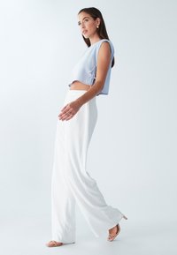 Lys blå cropped top med sidesnore, parret med løstsiddende hvide bukser. Hvide sko med en let hæl. Glat stofstruktur.