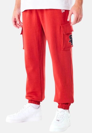 Røde cargo sweatpants med elastiske manchetter, prydet med to sidelommer og et sort broderet design på det højre ben. Sammen med hvide sneakers.
