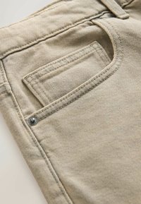 Nahaufnahme einer beige-farbenen Denim-Jeans-Tasche mit sichtbaren Nähten, Niete und Stoffstruktur.