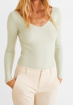 Haut long à manches ribbées vert clair avec un col en V, associé à un pantalon beige. Le tissu a une finition texturée, présentant une silhouette ajustée.